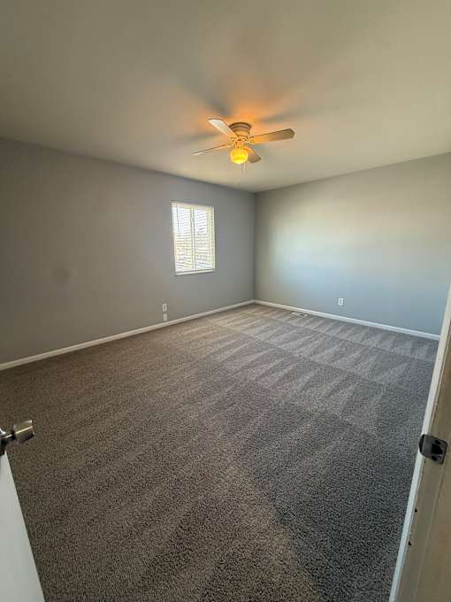 A ceiling fan with a light on in a room with a window.