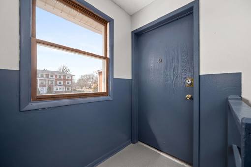 A room with a blue door and a window showing a view of a building outside.