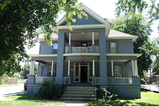 A two-story house with a front porch and a staircase leading to the entrance.
