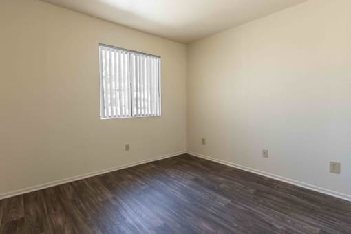 the living room of an empty home with wood flooring and a window