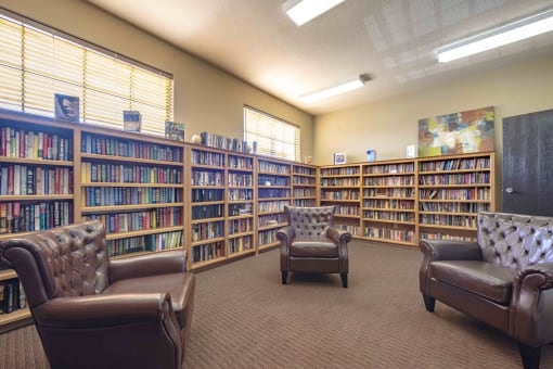 a library with brown leather chairs and bookshelves