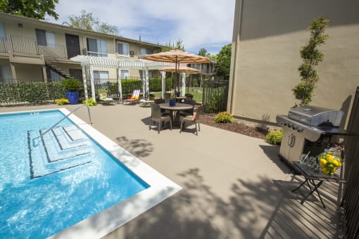 Pool area patio with a grill and a table and chairs at Abby Creek Apartments, Carmichael 