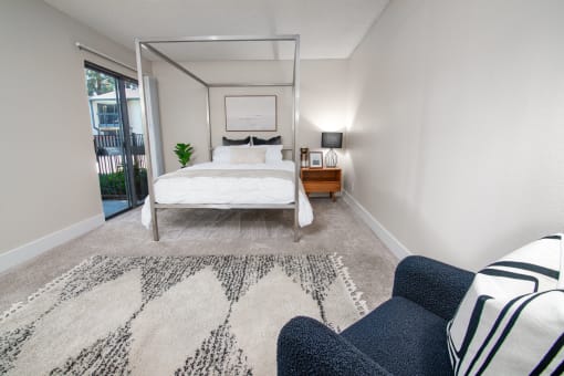 Model apartment bedroom with a bed, chair and rug, and patio door at at Rivercrest Apartments, Sacramento 
