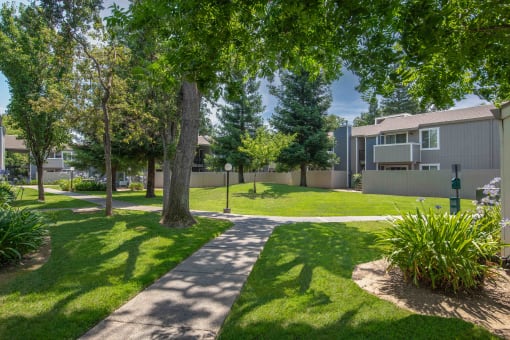 A sidewalk between apartment building with trees and grass and pet station at Willow Grove Apartments, California