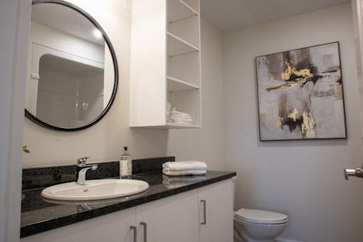 A bathroom with a sink, toilet, and a painting on the wall.