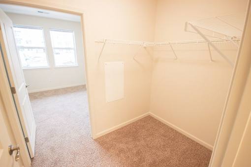 A small, empty room with a carpeted floor and a closet with shelves.