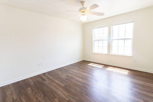 A room with a ceiling fan and two windows.