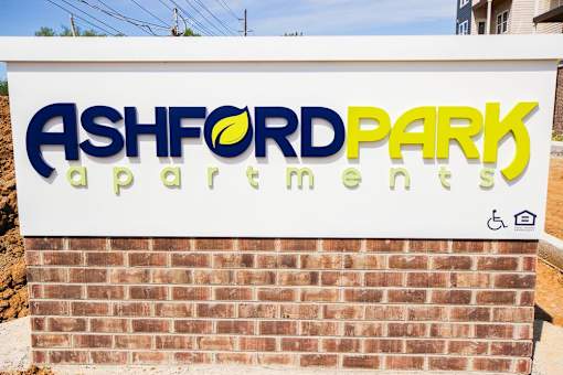A sign for Ashford Park Apartments is displayed on a brick wall.