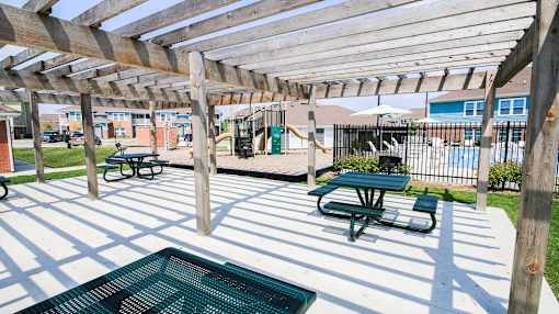A wooden pergola shades a picnic table in a sunny outdoor area.