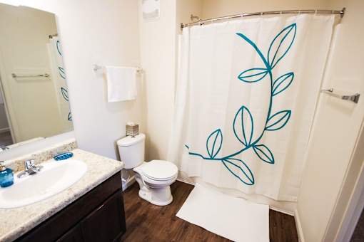 A bathroom with a white toilet and a shower curtain with blue leaves on it.