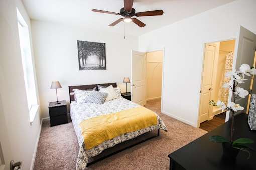 A bedroom with a bed, a ceiling fan, and a painting on the wall.
