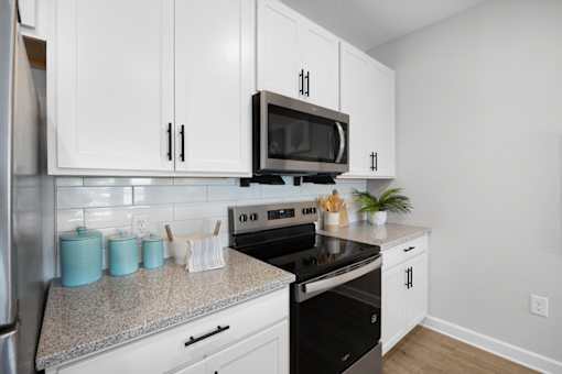 A kitchen with white cabinets and a black microwave above the stove.