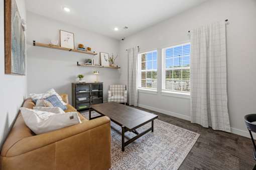 A living room with a tan couch, a wooden coffee table, and a window with curtains.