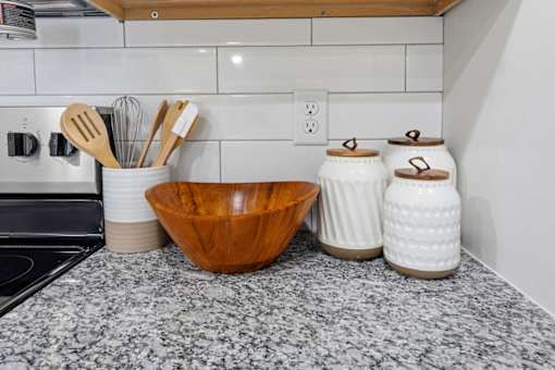A kitchen counter with a wooden bowl, white ceramic jars, and utensils.