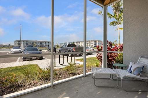 A patio with a chair and a table is overlooking a parking lot.