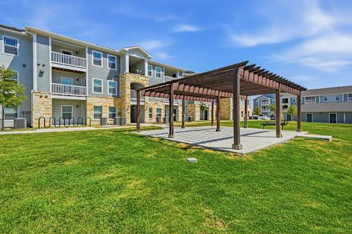 A sunny day at a grassy courtyard with a wooden pavilion and apartment buildings in the background.