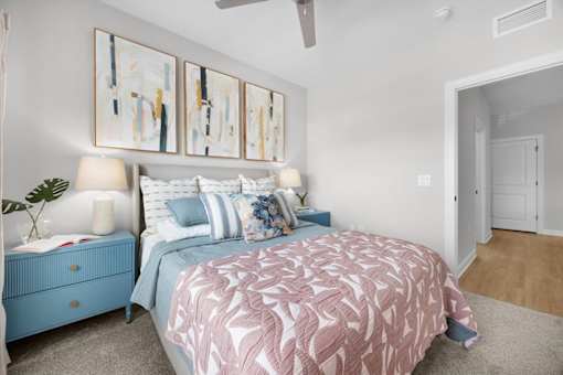 A bedroom with a pink bedspread and blue nightstand.
