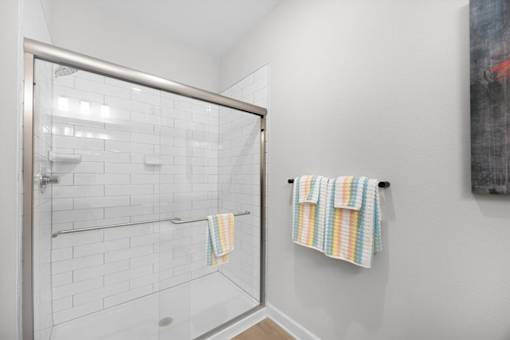 A white tiled shower with a glass door and a towel rack with two towels hanging on it.