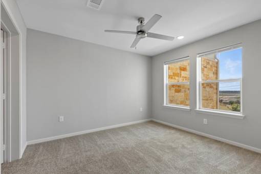 A room with a ceiling fan and two windows.