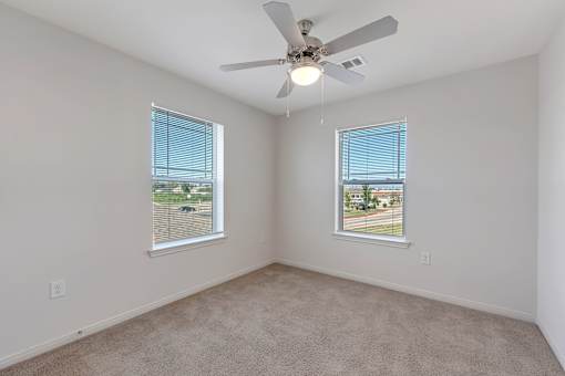 A room with a ceiling fan and two windows.
