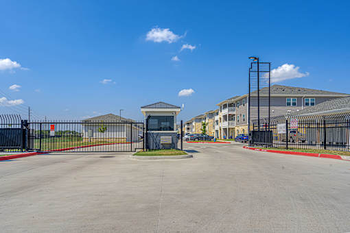 A gated community entrance with a guard booth and houses in the background.