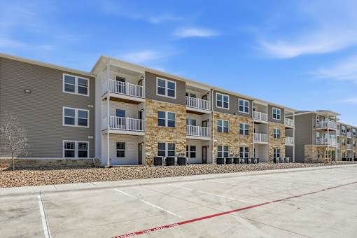 A row of modern apartment buildings with a parking lot in front.