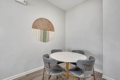 A white table with grey chairs is in front of a wall with a circular decoration.
