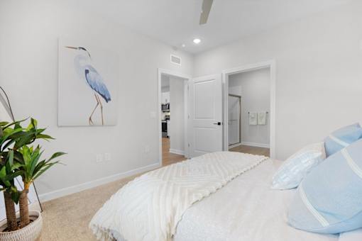 A bedroom with a bed, pillows, a ceiling fan, and a painting of a bird.