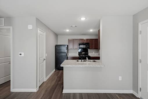 A kitchen with a black fridge and microwave, a white countertop, and brown cabinets.