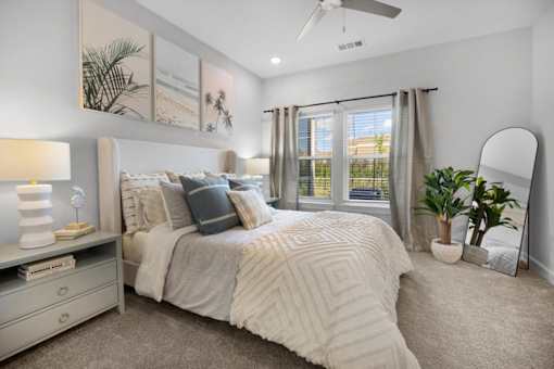 A bedroom with a large bed, a ceiling fan, and a window with curtains.