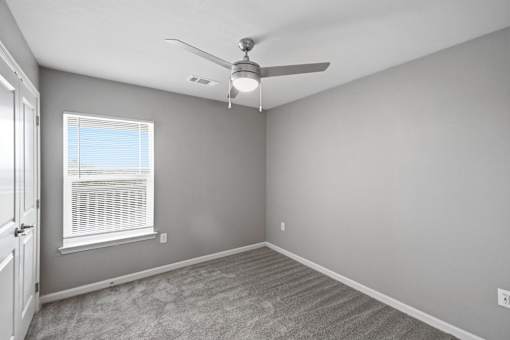 A room with a ceiling fan and a window with blinds.