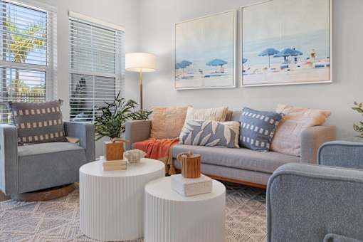 A living room with a grey couch, two grey armchairs, a white side table, and two paintings on the wall.