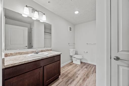 A bathroom with a sink, mirror, toilet, and wooden floors.