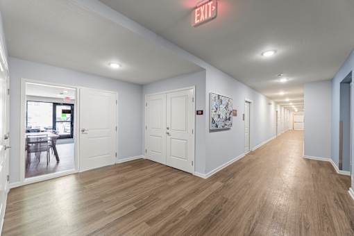 A long hallway with a red exit sign on the ceiling.