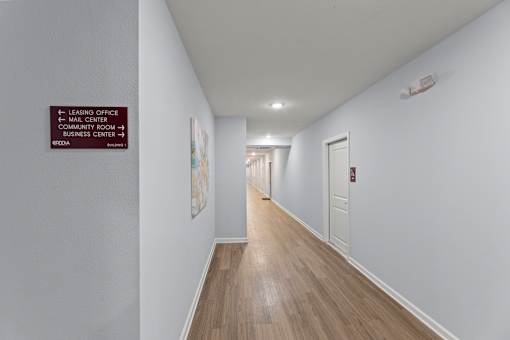 A long hallway with a sign on the wall pointing to the leasing office and mail center.