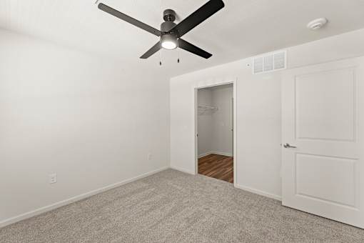 A room with a ceiling fan and a door leading to another room.