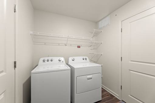 A laundry room with two washing machines and a shelf above them.