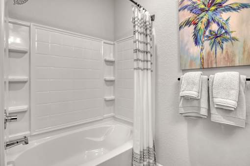 A white bathroom with a large tub and a painting of a palm tree.