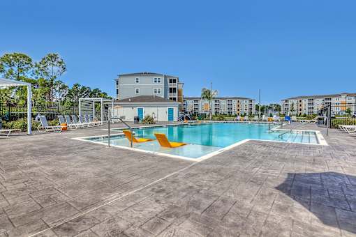 A large swimming pool surrounded by orange chairs and apartment buildings in the background.