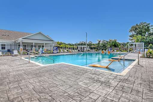 A large outdoor swimming pool with a sun lounger and a building in the background.