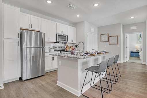 A kitchen with a refrigerator, microwave, and a counter with chairs.