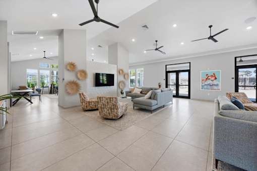 A spacious living room with a grey sofa, a white armchair, and a TV on the wall.