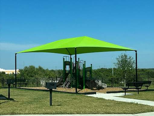 a green canopy over a playground at agave east apartments in del valle, texas