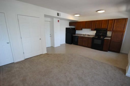 an empty living room with a kitchen in the background