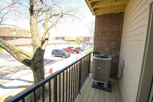 A balcony with a black railing and a tree in the background.