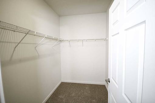 A white closet with a carpeted floor and a white door.