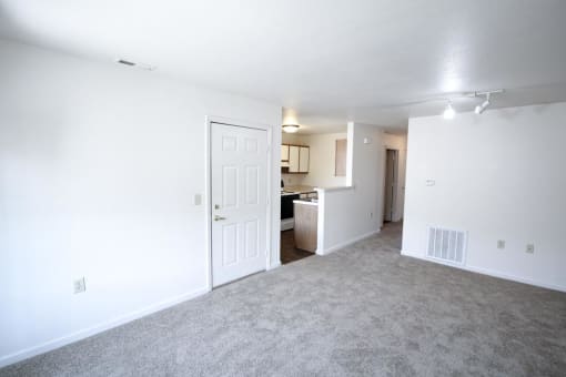 an empty living room with a kitchen in the background