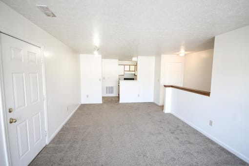an empty living room with a kitchen in the background