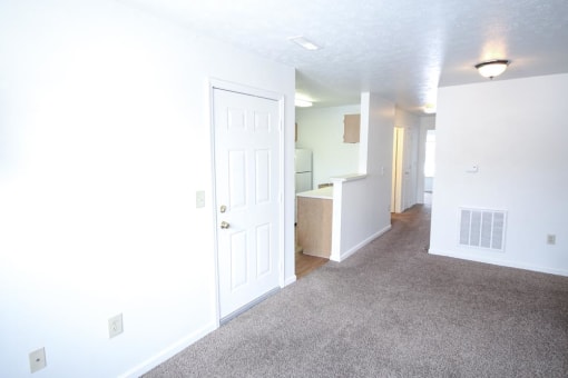 Empty living room with a white door and white walls at Conner Court apartments in Connersville, IN