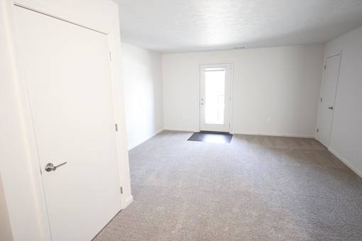 A white door is open to a room with a carpeted floor and white walls.
